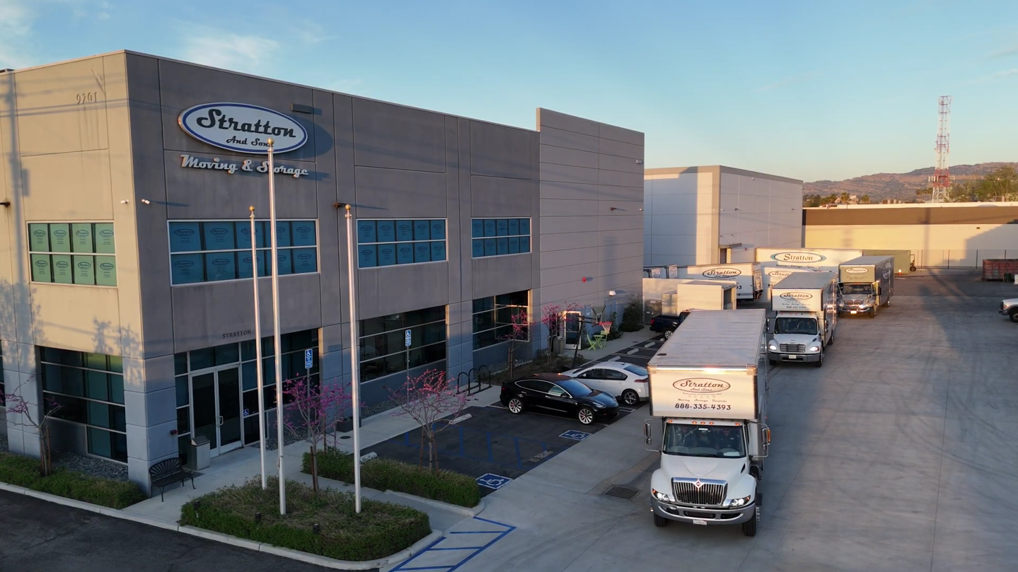 Aerial view of the Stratton and Sons Moving and Storage building in Chatsworth with the company sign and a fleet of branded moving trucks lined up outside